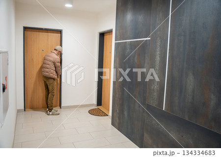 Man leaning near the door of an apartment corridor. Waiting or listening inside residential building. Man leaning near the door of an apartment corridor. Waiting or listening inside residential building. 134334683