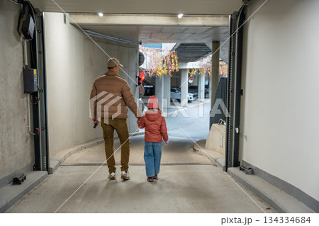 Man holding child's hand walking through garage entrance. Morning walk with child in residential area. 134334684