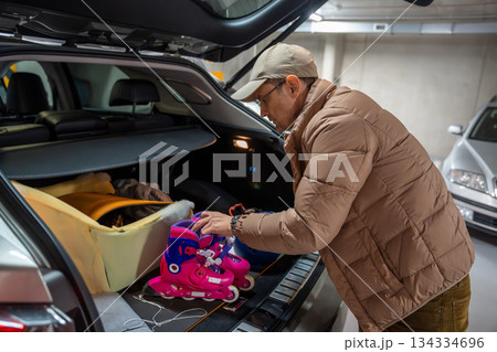 Man placing children's belongings into the car trunk. Preparation for family travel or daily routine. Man placing children's belongings into the car trunk. Preparation for family travel or daily routine. 134334696