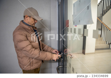Man unlocking the glass door to enter a stairwell. Routine entry into modern residential building. 134334699
