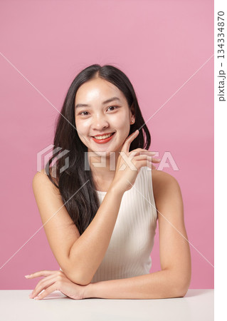 Skincare Routine. Young woman applying moisturizer with a radiant smile against a pink background. Skincare Routine. Young woman applying moisturizer with a radiant smile against a pink background. 134334870