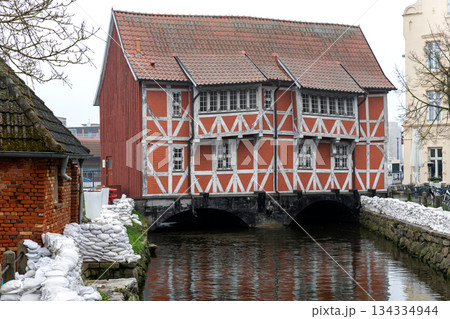 Sandbags line canal flood protection barrier historic Wismar town architecture timber facade building. Emergency safety infrastructure reinforces embankment stability high water risk overcast weather 134334944
