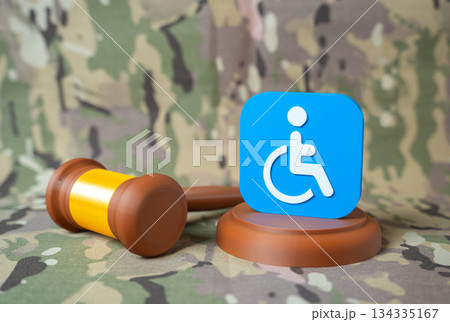 Judge's gavel and symbol of people with disabilities on military background. Assignment of disability status to seriously wounded personnel. Benefits and compensation for veterans and injured soldiers Judge's gavel and symbol of people with disabilities on military background. Assignment of disability status to seriously wounded personnel. Benefits and compensation for veterans and injured soldiers 134335167
