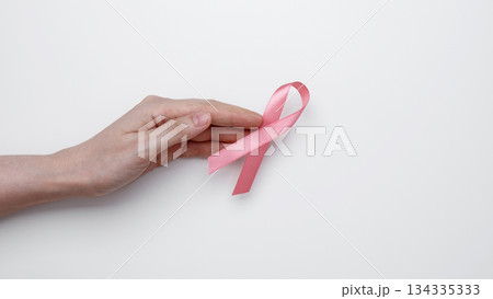 Symbol of breast cancer awareness. Woman hand holding pink ribbon 134335333