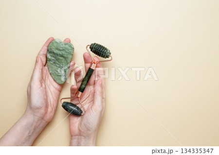 Female hands holding marble face roller and gua sha tools for skincare routine 134335347