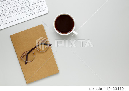 Cozy workspace with coffee cup, keyboard, glasses and notebook creating focused morning atmosphere 134335394