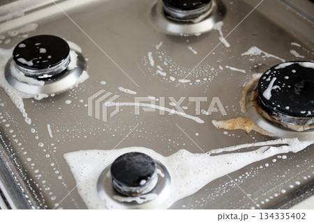 Cleaning dirty gas stove with foamy detergent in kitchen 134335402