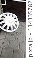 A dirty, white plastic wheel cover lies on a grey interlocking paved surface, resting against a dark wooden background and white pipes 134335782