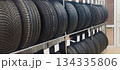 New automotive tires are neatly stacked on metal shelving in a tire shop or auto parts store, displaying various tread patterns and price tags 134335806