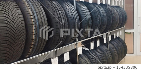 New automotive tires are neatly stacked on metal shelving in a tire shop or auto parts store, displaying various tread patterns and price tags 134335806