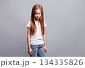 Moody angry young girl staring from under her brow, expressing hurt feelings, negative emotions while standing in studio, kids emotional portrait and facial expression on neutral background 134335826