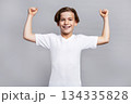 Young boy with happy face celebrating victory. Child expressing success and achievement. Kid showing strength and positive emotion in bright studio on grey isolated background 134335828
