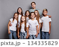 Group of happy children, boys and girls, standing together and smiling in studio against gray background. Beautiful kids wearing white t-shirts showing friendship, joy and positive emotions 134335829