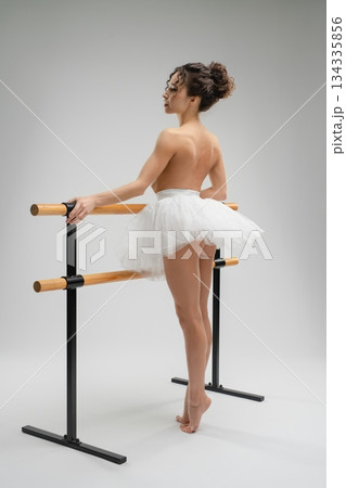 Elegant ballet dancer in nude pose with tutu by the barre in soft light 134335856