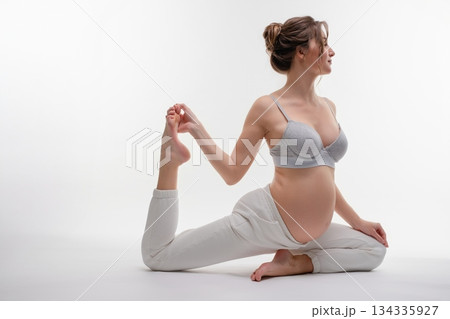 Pregnant woman practicing yoga poses indoors while wearing lingerie 134335927
