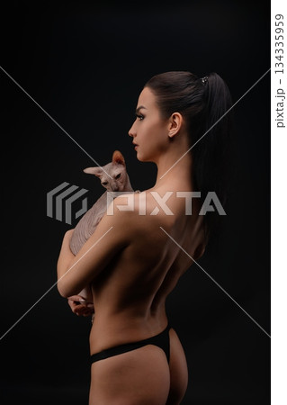 Woman holding a cat while showcasing natural beauty against a dark background 134335959