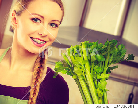 Woman in kitchen holds green celery Woman in kitchen holds green celery 134336691