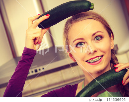Woman in kitchen holds zucchini vegetable Woman in kitchen holds zucchini vegetable 134336693