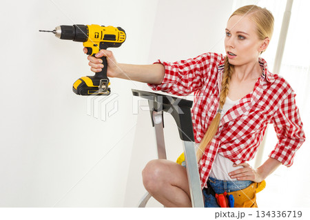 Woman using drill on ladder Woman using drill on ladder 134336719