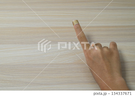 木目調のテーブルと絆創膏を貼った指 134337671