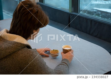 Young caucasian man holding paper cup and looking out large cafe window at city street, enjoying quiet moment indoors. Coffee Break. Cozy winter. Young caucasian man holding paper cup and looking out large cafe window at city street, enjoying quiet moment indoors. Coffee Break. Cozy winter. 134338027