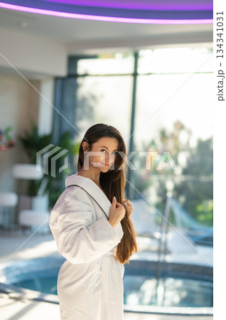 Woman in white bath robe standing near the pool in a spa center 134341031