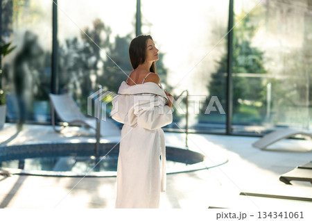 Woman in white bath robe standing near the pool in a spa center Woman in white bath robe standing near the pool in a spa center 134341061