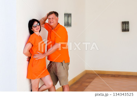 An adult man and woman in orange clothes are hugging tenderly An adult man and woman in orange clothes are hugging tenderly 134343525