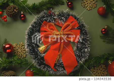 Festive Christmas wreath with red bow and ornaments on green background Festive Christmas wreath with red bow and ornaments on green background 134343530