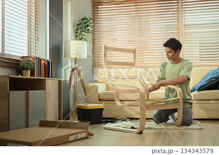 A man assembling new rocking armchair at home with screwdriver, DIY home improvement A man assembling new rocking armchair at home with screwdriver, DIY home improvement 134343579