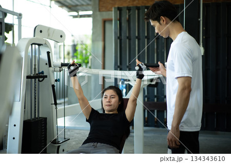 Woman lifting weight machine with trainer guidance Woman lifting weight machine with trainer guidance 134343610