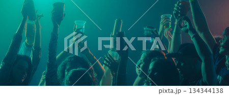 People raising drinks and hands during night celebration. Banner People raising drinks and hands during night celebration. Banner 134344138