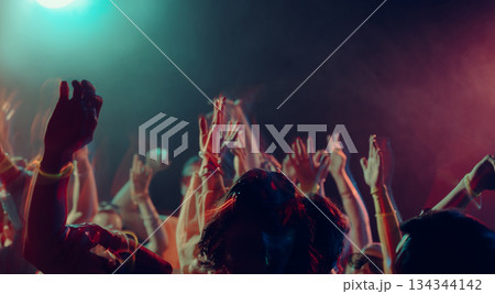 Nightclub crowd celebrating together in colorful light. 134344142