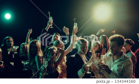 Festive crowd raising champagne glasses under bright party lights 134344160