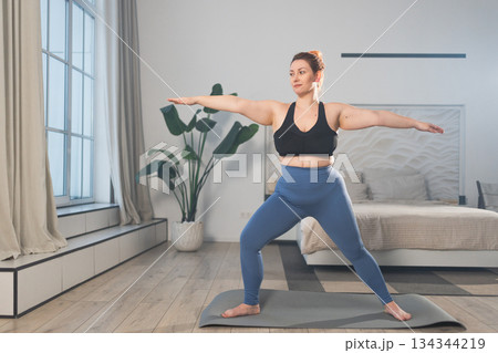 Yoga fitness workout training. Woman practicing yoga at home. Plus size female doing sports exercise on yoga mat indoor. Girl in sportswear have training workout for weight loss. Sport and fitness Yoga fitness workout training. Woman practicing yoga at home. Plus size female doing sports exercise on yoga mat indoor. Girl in sportswear have training workout for weight loss. Sport and fitness 134344219