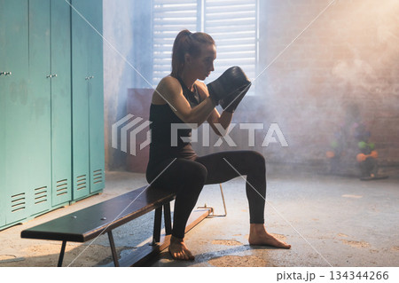 Workout in gym. Woman fighter ready for fight punching with boxing gloves in locker room. Strong girl training punches preparing for boxing sparring active exercise workout training in gym Workout in gym. Woman fighter ready for fight punching with boxing gloves in locker room. Strong girl training punches preparing for boxing sparring active exercise workout training in gym 134344266