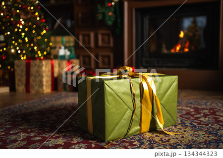 Green gift box in classical Christmas decorated interior living room library with fireplace. Christmas gift near fir tree on Christmas eve. Modern classic style interior design apartment. Christmas Green gift box in classical Christmas decorated interior living room library with fireplace. Christmas gift near fir tree on Christmas eve. Modern classic style interior design apartment. Christmas 134344323