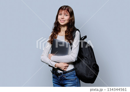 Portrait of beautiful girl teenage student with backpack, laptop on gray background 134344561