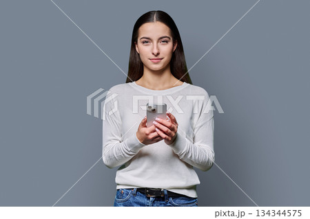 Portrait of serious teenage girl holding smartphone on gray studio background 134344575