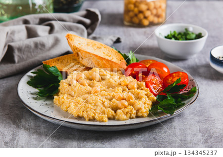 Chickpea puree, tomatoes, toast and greens on a plate on the table 134345237