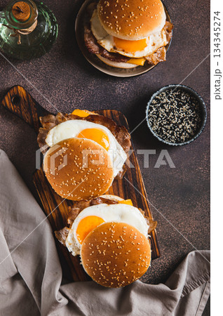 Breakfast sandwich with egg, bacon and cheese on a board on a table top and vertical view 134345274