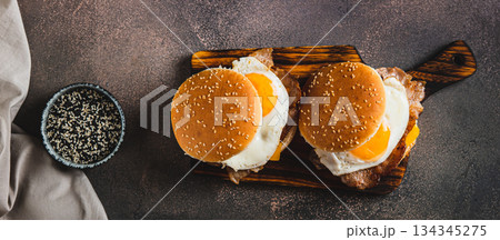 Breakfast sandwich with egg, bacon and cheese on a board on a table top view web banner 134345275