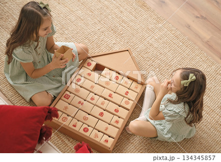 Children open another box of the New Year's Advent calendar sitting on the floor. Happiness in anticipation of winter holidays and miracles. There's a surprise in every box. 134345857