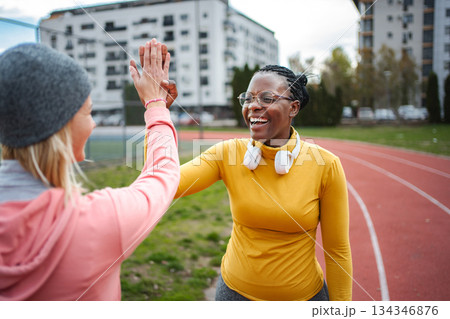 Women high-fiving on running track celebrating success Women high-fiving on running track celebrating success 134346876