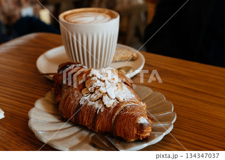 Delicious almond croissant with a latte in a cozy cafe setting Delicious almond croissant with a latte in a cozy cafe setting 134347037