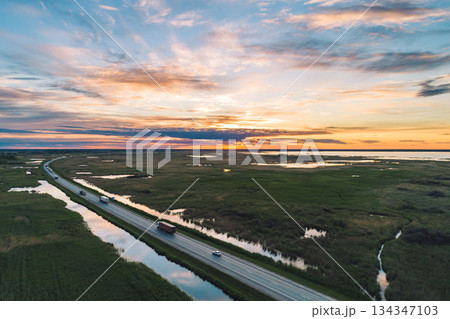 Vehicles travel along a highway through the green countryside at sunset Vehicles travel along a highway through the green countryside at sunset 134347103