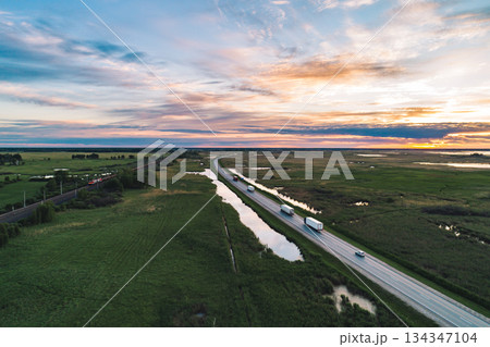 Vehicles travel along a highway through the green countryside at sunset Vehicles travel along a highway through the green countryside at sunset 134347104