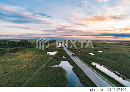Vehicles travel along a highway through the green countryside at sunset 134347105