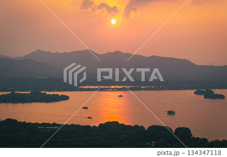 Aerial view of an orange sunset over West Lake and Hangzhou city with distant mountain. Aerial view of an orange sunset over West Lake and Hangzhou city with distant mountain. 134347118