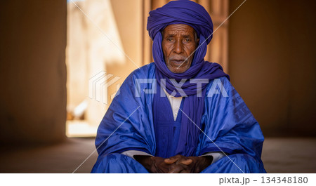 In a quiet space, a man from Mauritania sits calmly, stroking his beard as he listens closely to something. The light and shadows create a warm atmosphere around him. In a quiet space, a man from Mauritania sits calmly, stroking his beard as he listens closely to something. The light and shadows create a warm atmosphere around him. 134348180